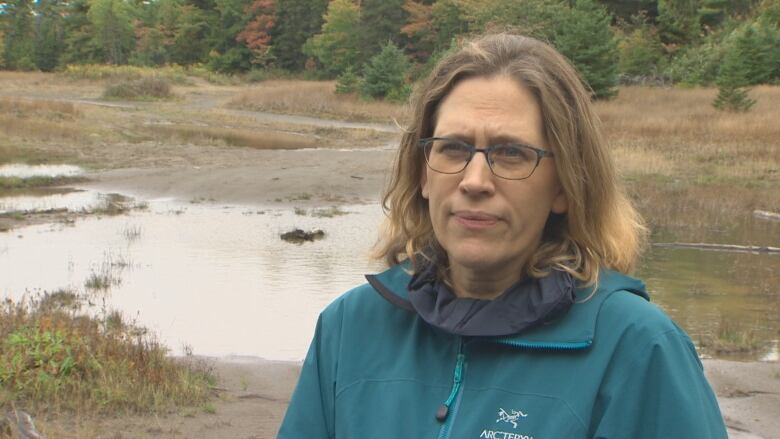 A woman is shown standing in front of a small pond.