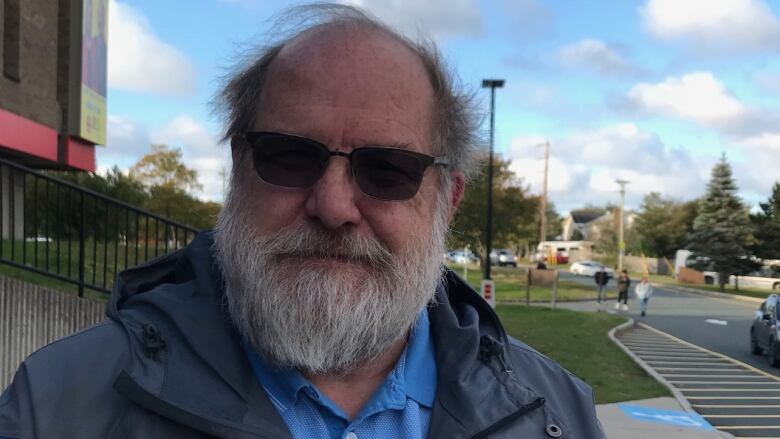 A smiling man with a grey beard and sunglasses sits outside the CBC studio in St. John's.