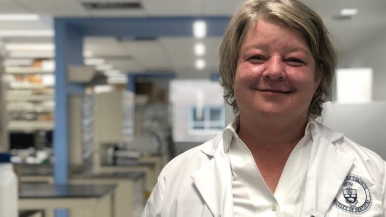 Woman wearing white lab coat, smiling.