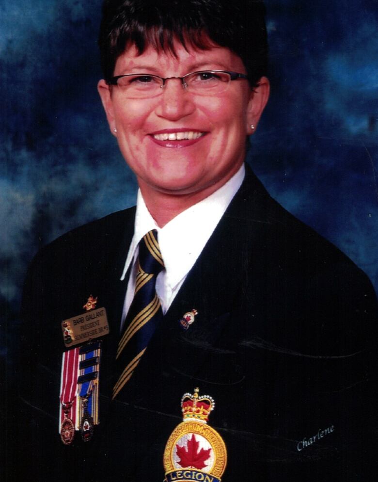 A woman with glasses and short brown hair poses in a Royal Canadian Legion uniform. 