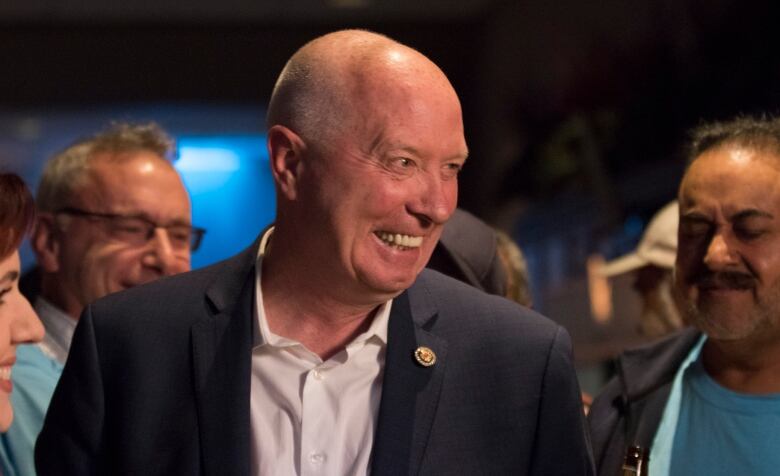 Burnaby mayor Mike Hurley smiles at someone off-camera. There are people smiling in the background.