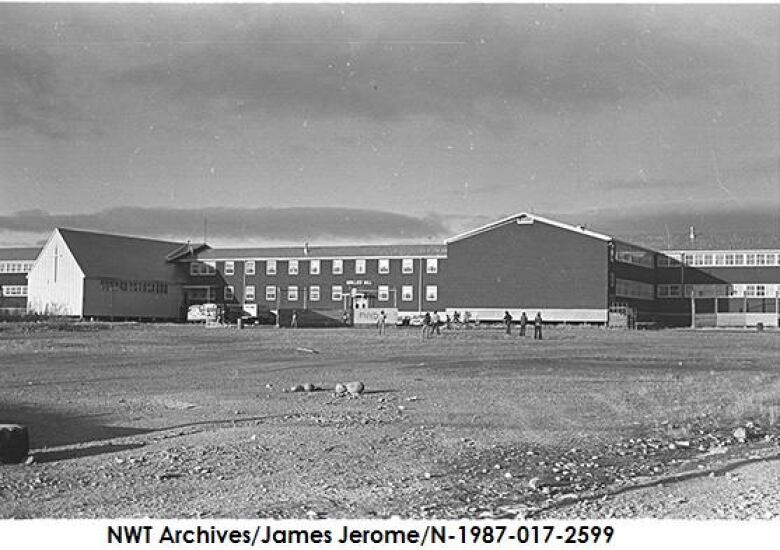 Black and white photo of a large two-story building on a very flat landscape.