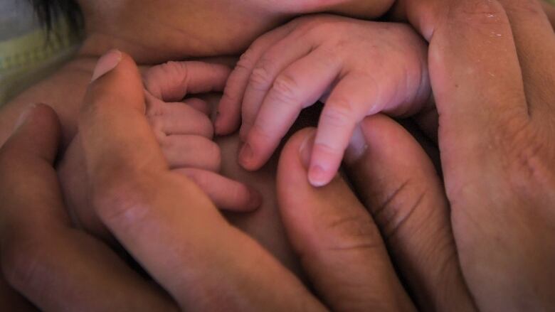 A photograph shows an unidentifyable person holding the hands of a newborn baby. 