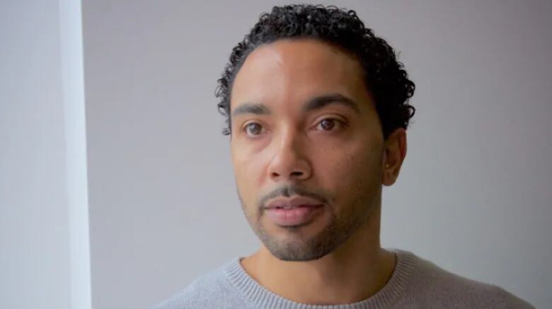 A head shot of a Black man who is wearing a grey sweater.