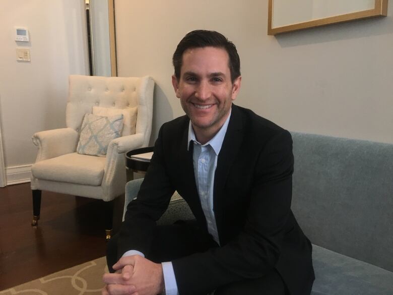 Man smiles in blazer sitting on couch