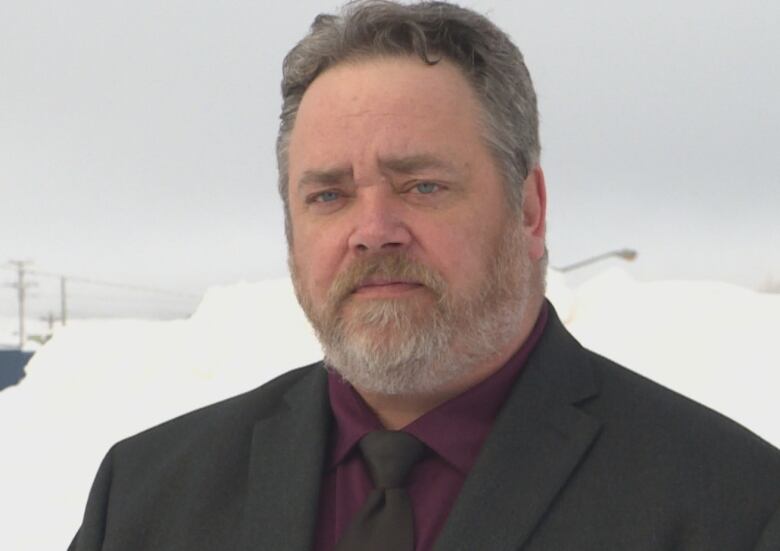 A man wearing a suit stands in front of a snow bank.