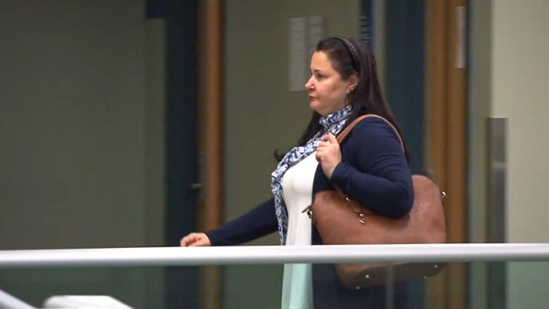 Woman walks in a courthouse with a handbag over her shoulder.