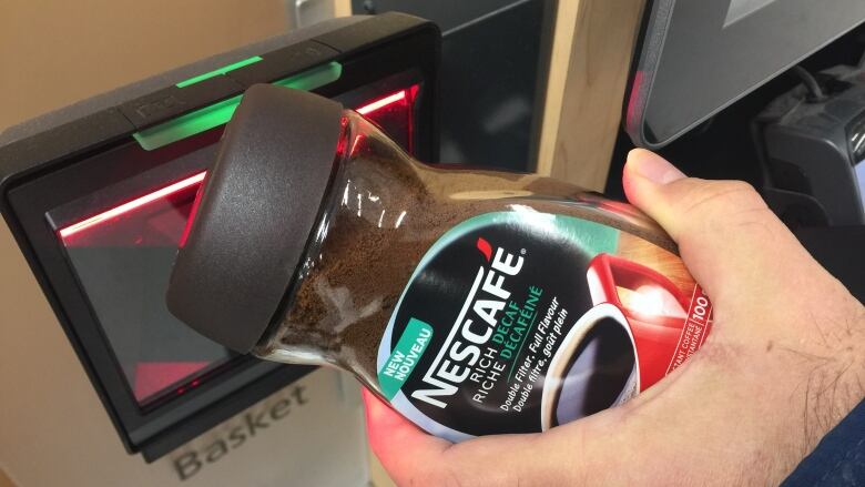 A hand scanning a jar of instant coffee at self-checkout