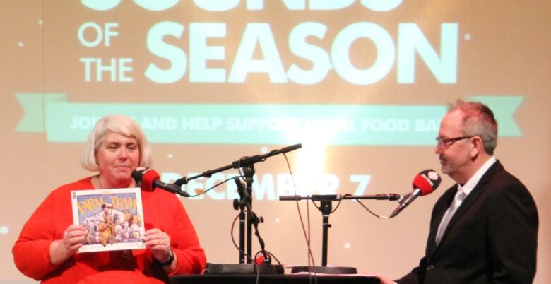 A woman holds up a book during an interview with the male host on stage