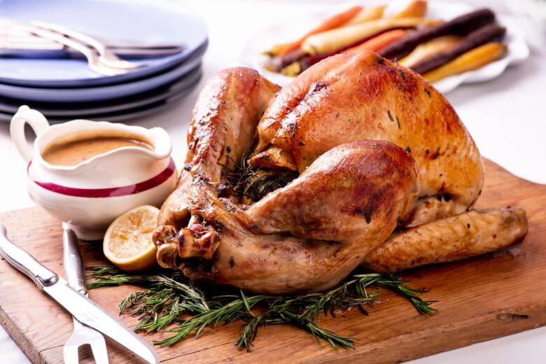 Closeup on a roasted turkey sitting on a wooden cutting board with a small dish of gravy next to it, all sitting on a table. 