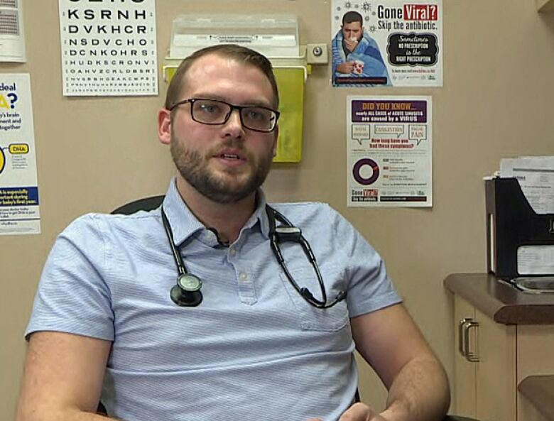 Man in blue collared shirt with glasses sits in doctors office.