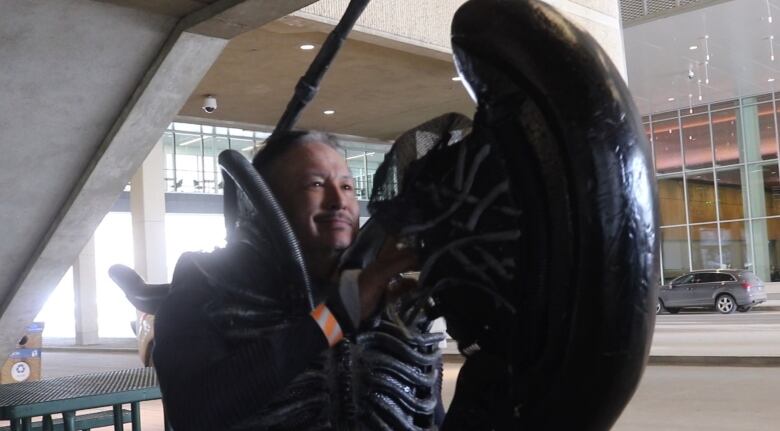 A smiling man wears an alien costume.