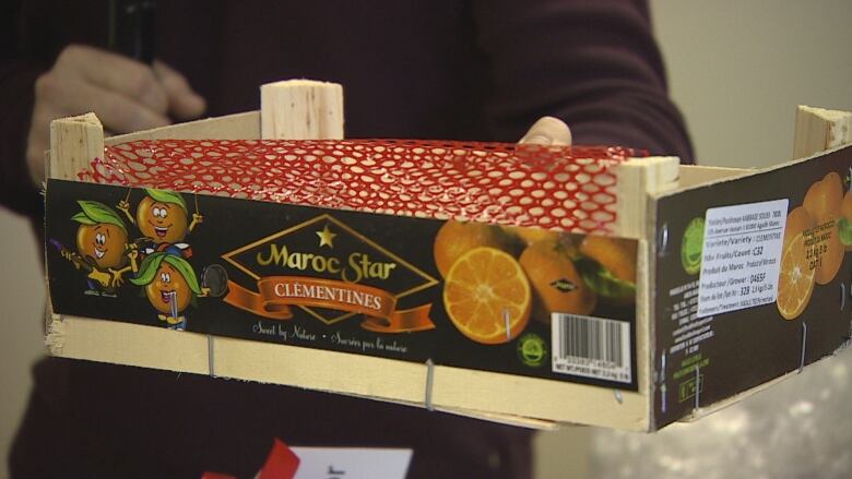 A hand holding a wooden box with a clementine label on the side.