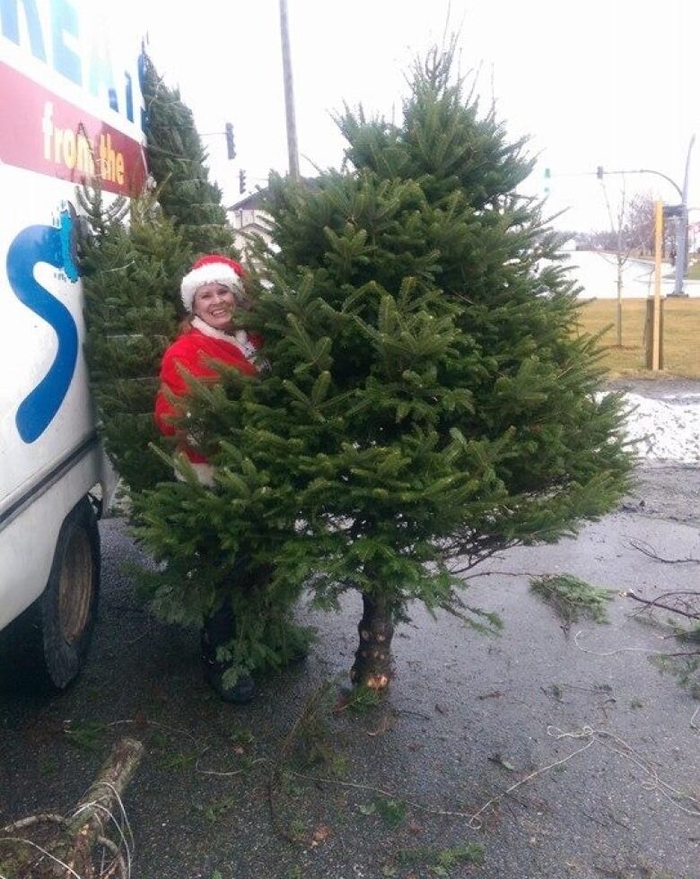 Woman holds a large Christmas tree in parking lot. 