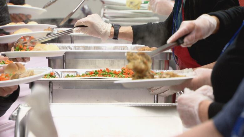 Closeup on hands wearing surgical gloves serving a row of people holding plates.