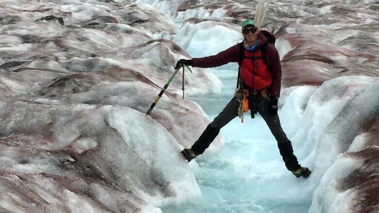 A man stretches his legs across a crevice in a glacier. 