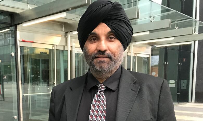 A Sikh man wearing a black turban smiles for the camera.