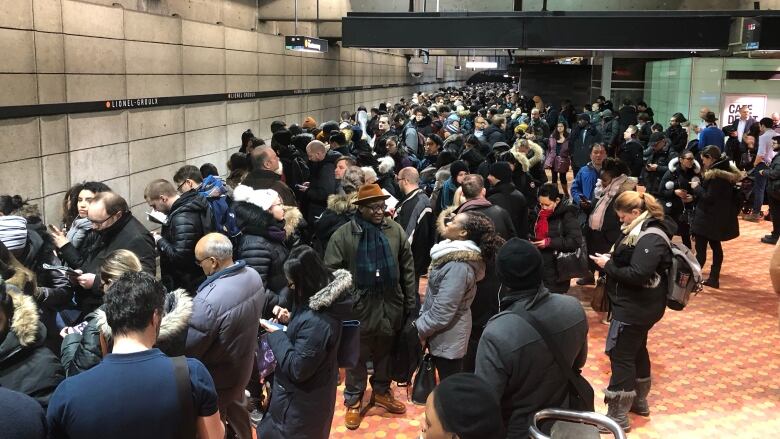 A crowd of frustrated-looking people stand on the Metro platform.