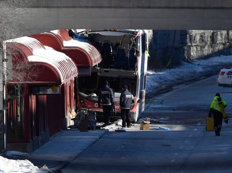 Two men in black jackets look at a damaged bus. 