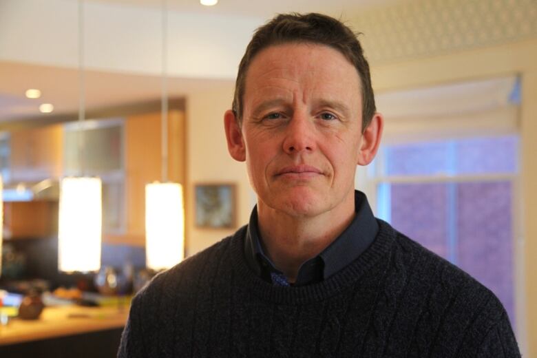 A man with brown hair, a black sweater and a blue collared shirt.