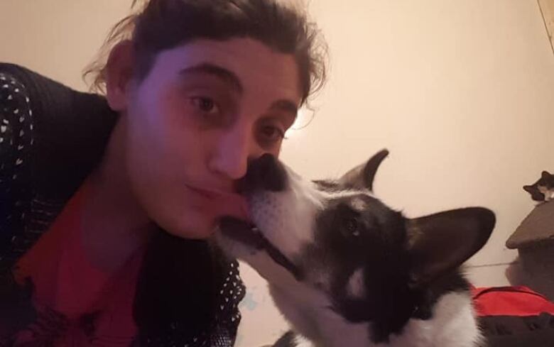 A woman looks at the camera as her dog gives her a nuzzle on the cheek. 