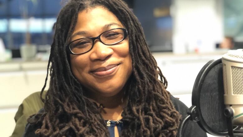 A Black woman smiles as she sits behind a microphone in a radio studio.