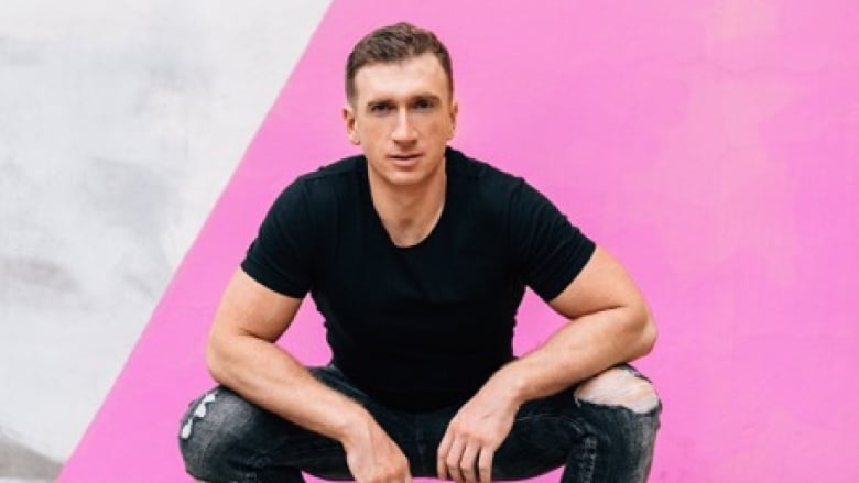 A man sits in front of a white and pink background