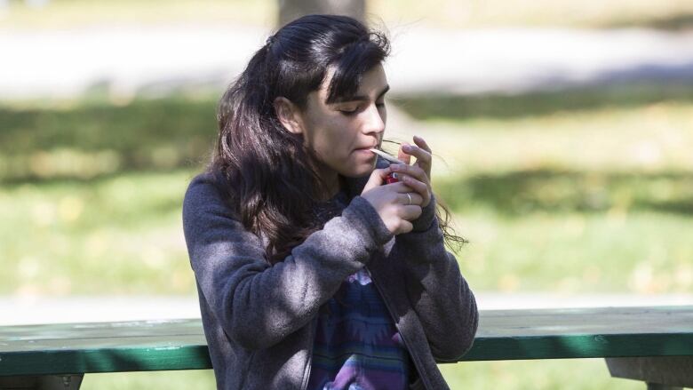 A woman smoking a joint on a park bench.