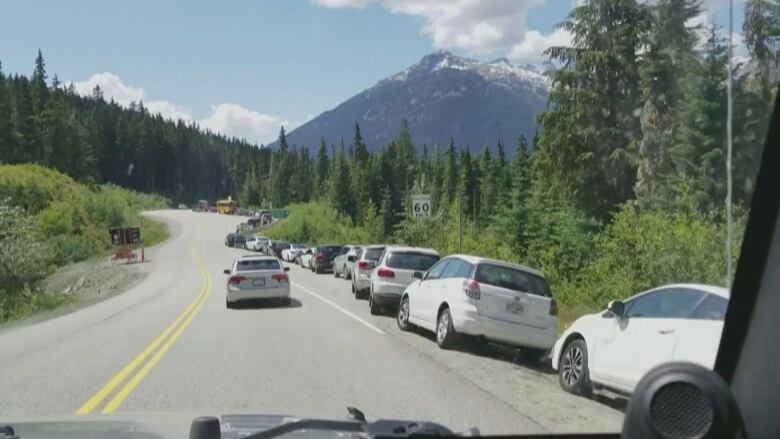 Cars lined up on the side of a highway with mountains in the background.