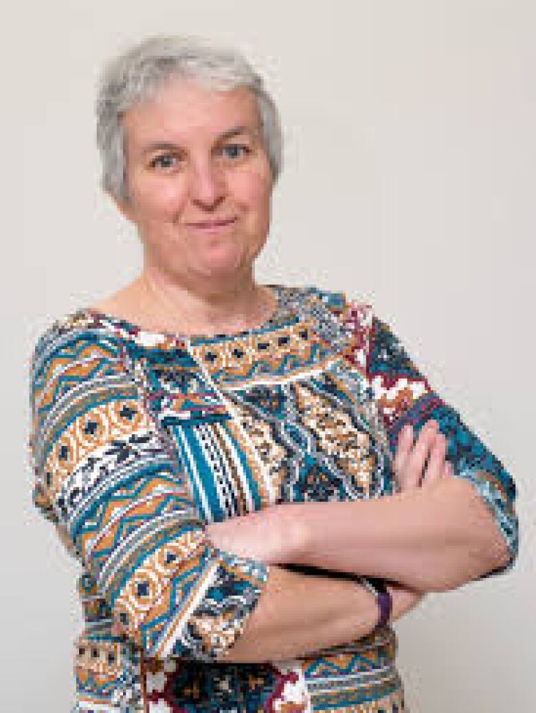 A woman wearing a colorful top can be seen folding her arms and smiling. 