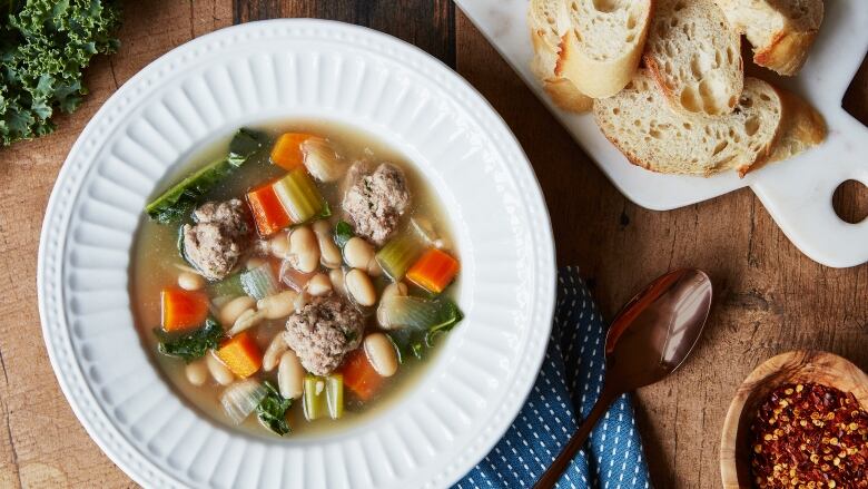 Overhead shot of a shallow white bowl filled with meatball soup with lots of vegetables in it. It's sitting on top of a dark blue cloth napkin on a wooden table. 