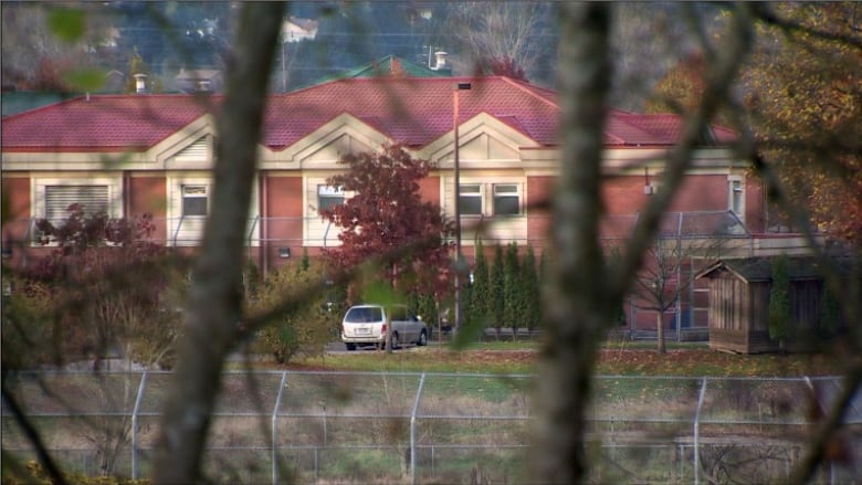 A picture of the forensic psychiatric hospital behind tree cover. It is behind a tall steel fence and has a red brick exterior.