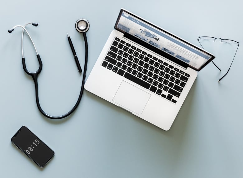 A stock overhead image of a laptop, glasses and a stethoscope.