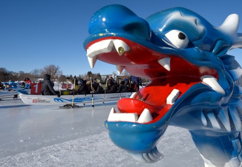 A blue dragon on the front of a boat about to race on an icy canal.