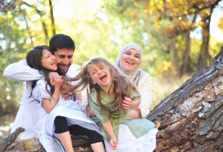 A Muslim couple and their two daughters laugh and hug in a forest.