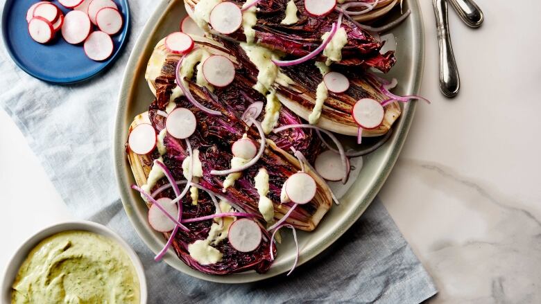 Overhead shot of a platter of grilled radicchio topped with red onion, radish slices and tahini sauce. 