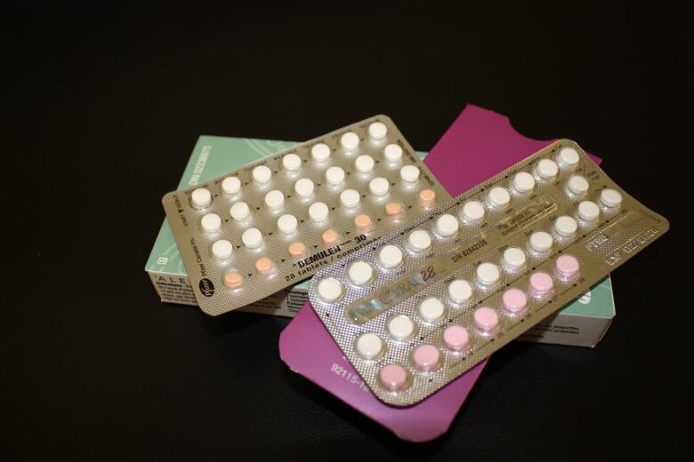 A package of birth control pills is seen on a black surface.