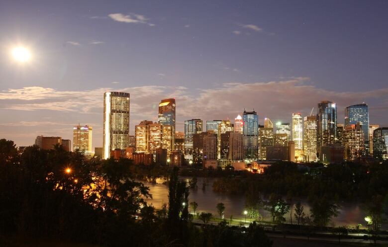 a view of calgary's skyline with a purple-blue sky behind it. the sun is setting