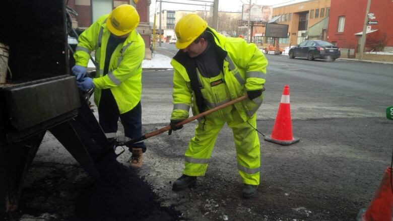 Two city workers fix a pothole.