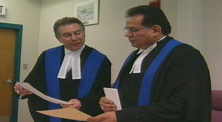 Judge Gerald Morin is sworn-in as a provincial court judge with another man in the room while they look at a piece of paper