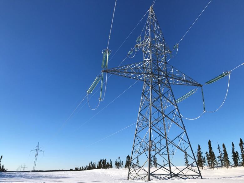 A steel electrical tower in the middle of a snowy field on a clear day.