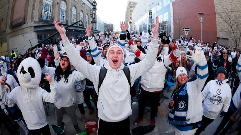  A crowd of hockey gans in white shirts and sweaters on a street outside Canada Life Centre.