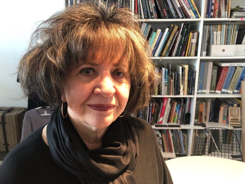 A woman poses for a photo in front of a shelf lined with books.