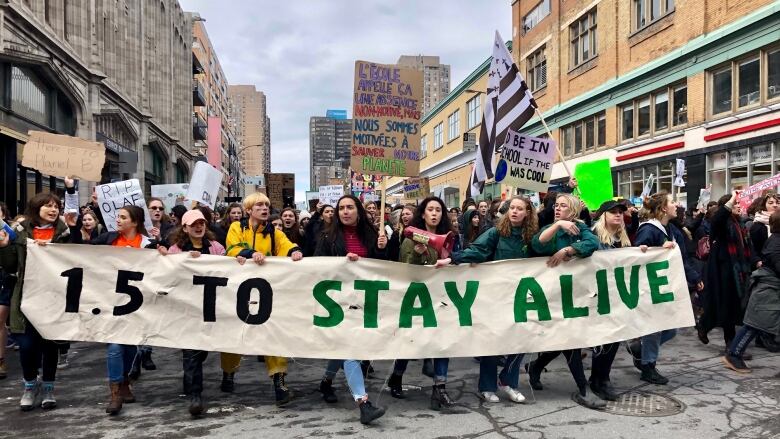 Students carrying a banner reading '1.5 to stay alive' march down a street in downtown Montreal.