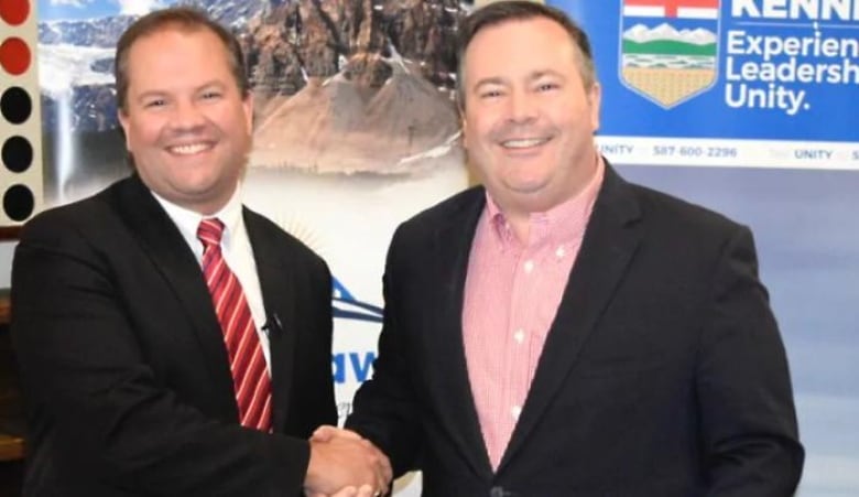 Two men look at the camera as they shake hands.