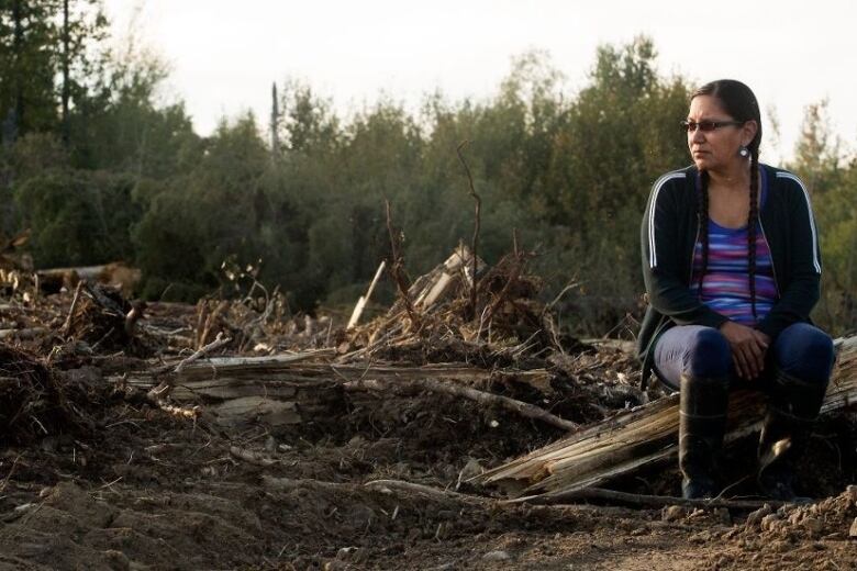 a woman sits on broken wood from a fallen tree