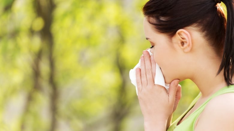 A woman outdoors holds her nose in a tissue.