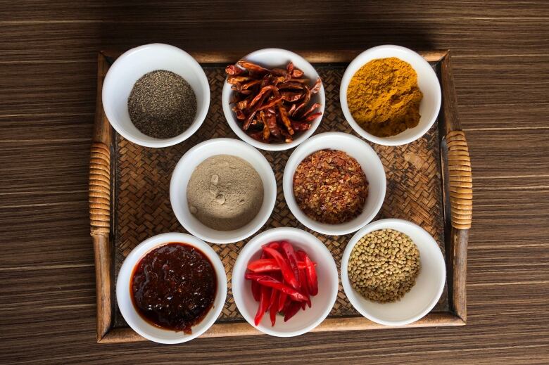 A wooden tray filled with eight small bowls of a variety of spices.