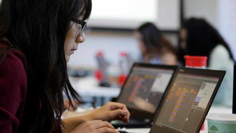 A teenage girl with black hair wearing a red shirt and glasses working on a laptop computer