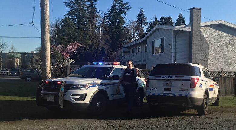 A police officer poses by two vehicles parked outside a home.